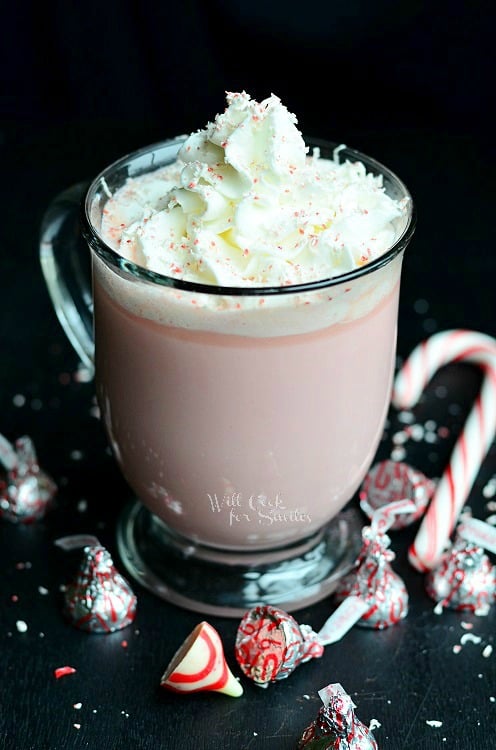 Peppermint White Hot Chocolate in a clear mug with candy canes and peppermint kisses around it 