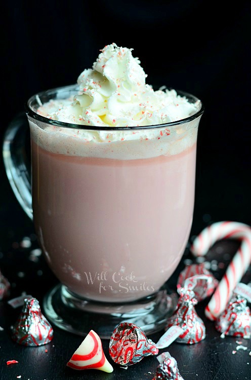 Peppermint White Hot Chocolate in a clear mug with candy canes and peppermint kisses around it 