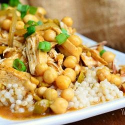 close up view of moroccan chicken dish on white rectangular plate with for to the right on wood table with brown napkin above