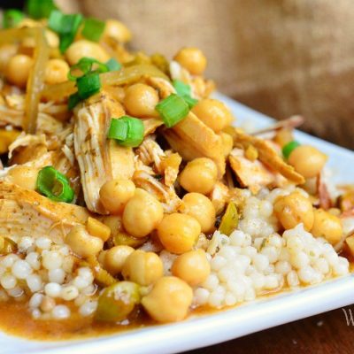 close up view of moroccan chicken dish on white rectangular plate with for to the right on wood table with brown napkin above