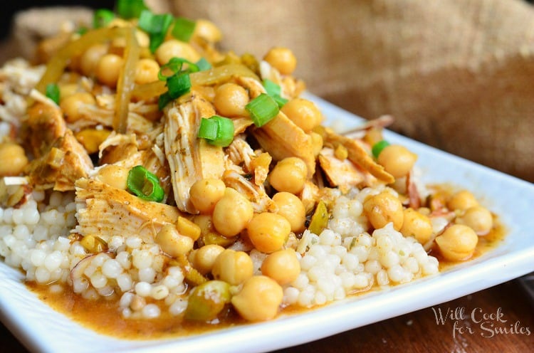 close up view of moroccan chicken dish on white rectangular plate with for to the right on wood table with brown napkin above