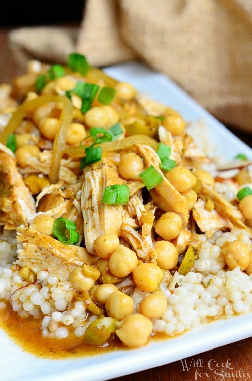 moroccan chicken dish on white rectangular plate with for to the right on wood table with brown napkin above