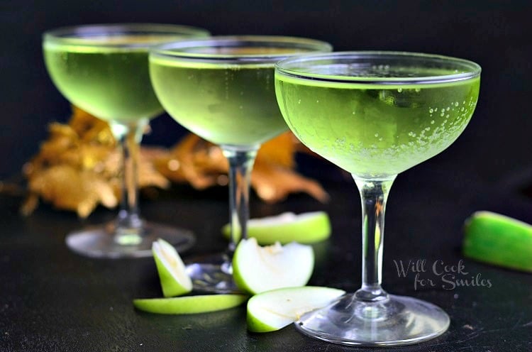 three green Sour Apple Champagne cocktails in wine glasses with green apples slices around the bottom 