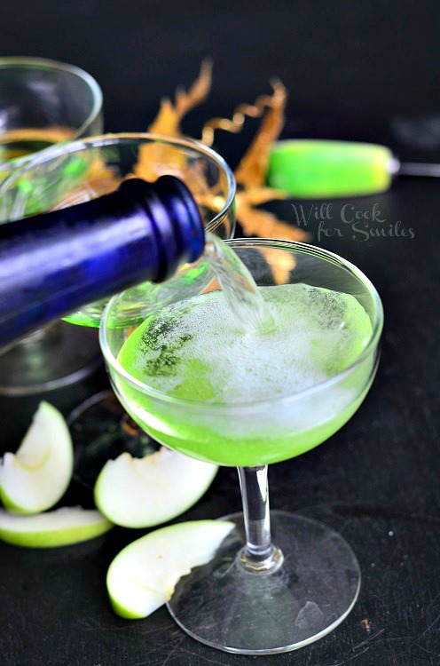 pouring Champagne into the cocktail glass in a wine glass with green apples slices around the bottom 