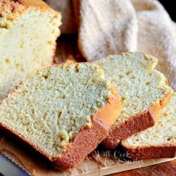 slice of vanilla bean eggnog bread on wood cutting board in front of rest of loaf and brown cloth in background and knife in bottom left