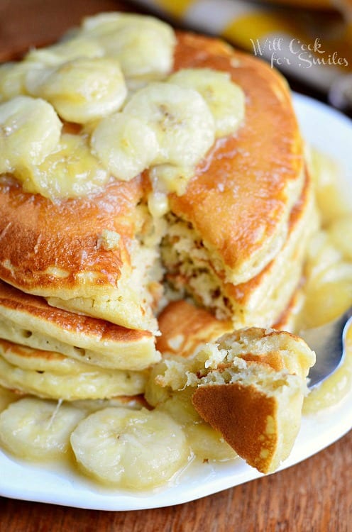 Bananas Foster Pancakes with sliced bananas on top on a white plate with a bite on a fork 