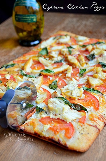 caprese chicken pizza on a wood cutting board with a pizza slicer slicing it 