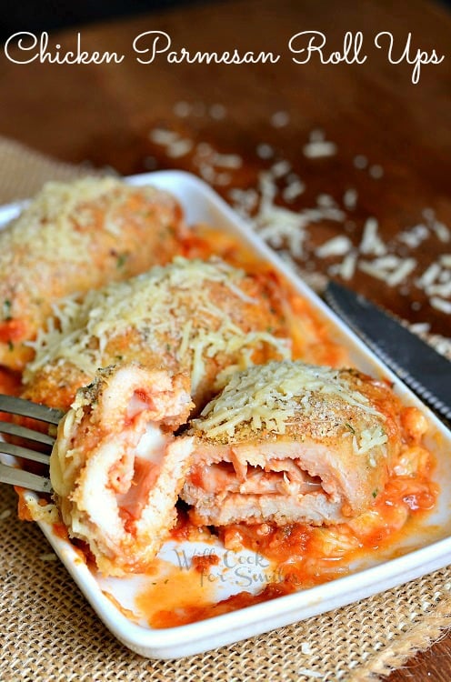 Chicken Parmesan Roll Ups with one cut in half and a fork lifting a piece up on a white serving plate 