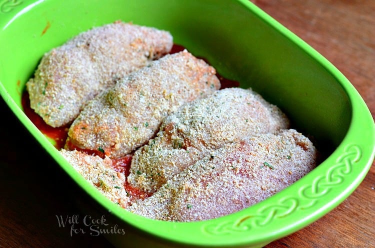 breaded chicken pieced with stuffing rolled up in a green baking dish with marinara sauce underneath