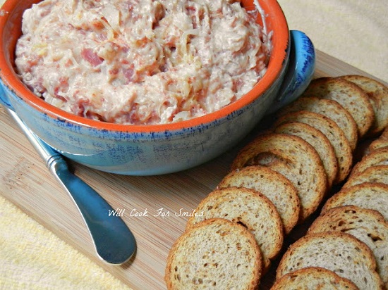 Ruben dip in a blue bowl on a wood cutting board with rye bread sliced next to it 