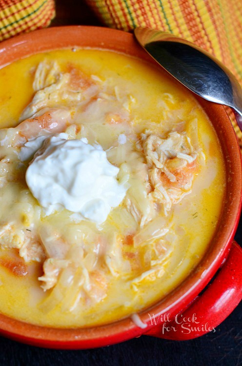 Creamy Chicken Enchilada Soup with a dollop of sour cream on top in a red bowl with a spoon  on the right 
