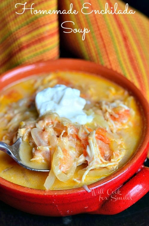 Enchilada Soup in a red soup bowl with chicken and onions and a dollop of sour cream on top scooping some out with a spoon 