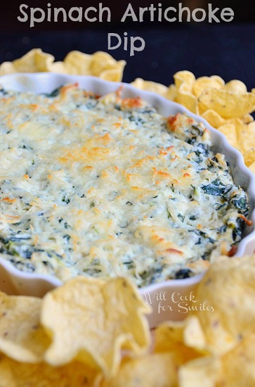 spinach artichoke dip in a white bowl with tortilla chips around it 