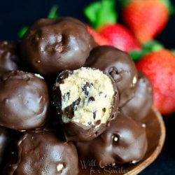 brown bowl with no bake chocolate covered peanut butter cheesecake bites on a black table with strawberries to the right of bowl