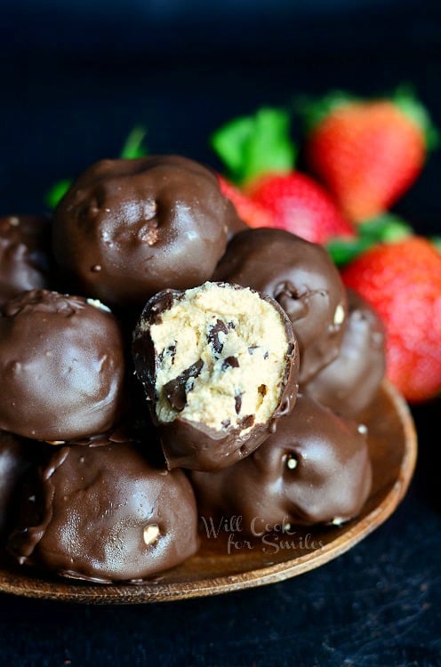 Chocolate Covered Peanut Butter Cheesecake Bites on a wood bowl with strawberries in the background 