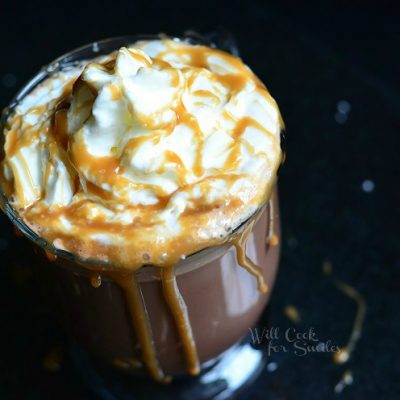 view from above of glass coffee mug filled with skinny salted caramel hot chocolate on a black table. Hot chocolate is topped whipped cream and caramel drizzle running down the side of the glass