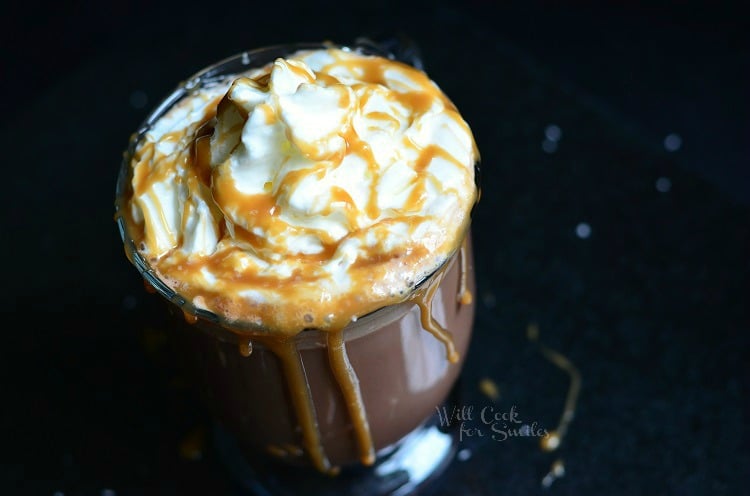 above photo Caramel Hot Chocolate with whip cream and caramel sauce on top and caramel sauce coming over the sides 