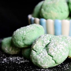 close up view of blue and pink bowl filled with cotton candy cookies on a black table and 4 cookies on table in front of bowl all dusted with powdered sugar