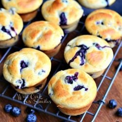 batch of vanilla blueberry muffins on cooling rack with blue berries below