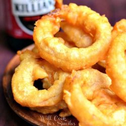 view from above of fried beer batter onion rings in a wood bowl on a wood table with bottle of killians in background