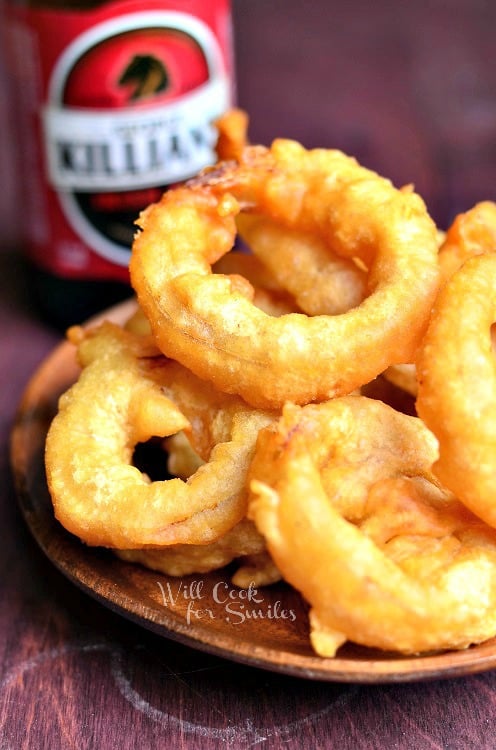 A pile of Beer Batter Onion Rings served on a wooden plate.