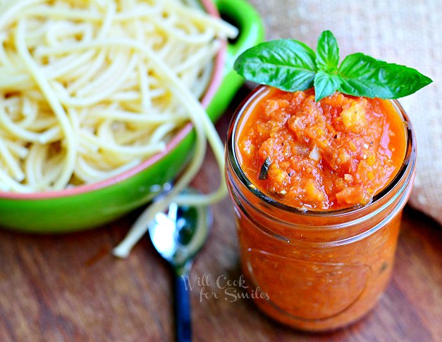 Marinara Sauce with basil on the side and a bowl of pasta in the background 