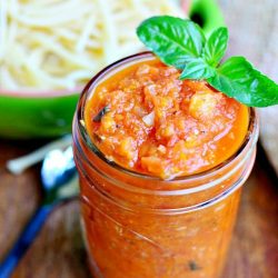 clear glass mason jar filled with home made marinara sauce on wood table with bowl filled with pasta in background to the left