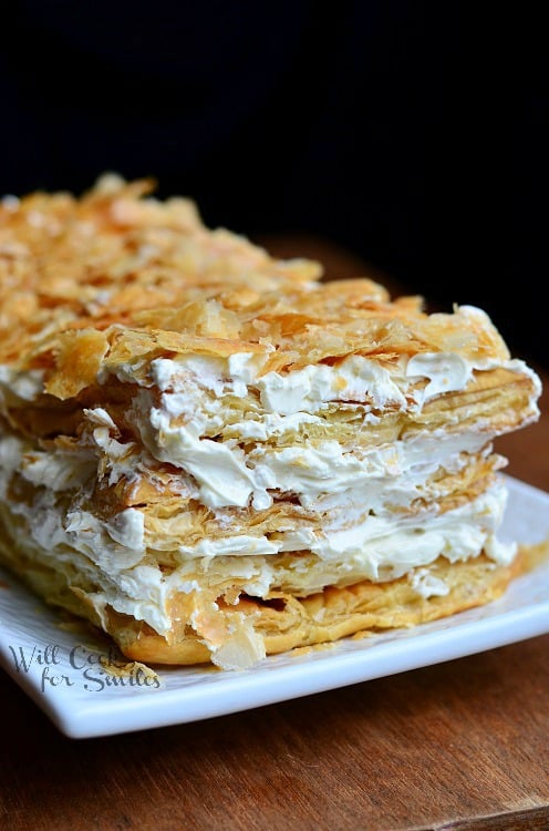 close up view of 1 portion of napoleon cake on a white rectangular plate on wood table with black background