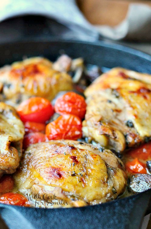 closer side view of chicken thighs with tomatoes and mushrooms in a skillet