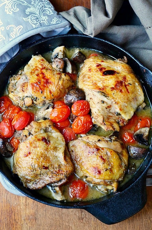 top view of four chicken thighs in a skillet with mushrooms and cherry tomatoes