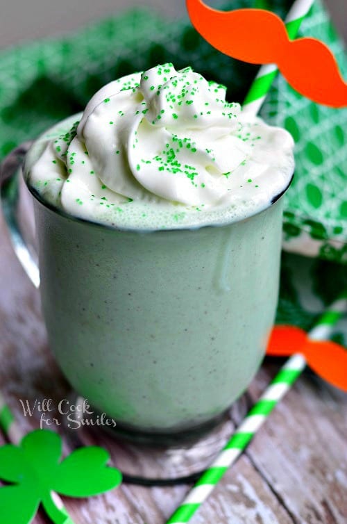 St. Patrick's Day Milkshake in a glass cup with whip cream and green sprinkles on top with a green and white straw