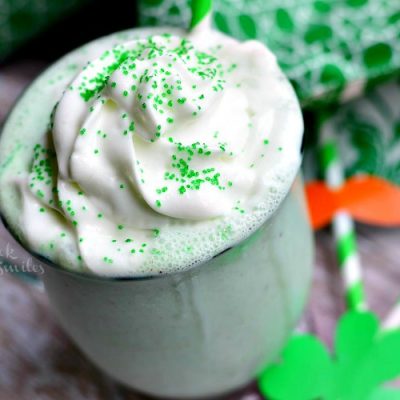clear glass coffee mug filled with st patrick's day skinny milkshake creamy mint chocolate chip on a wood table with st patties day decore scattered on table