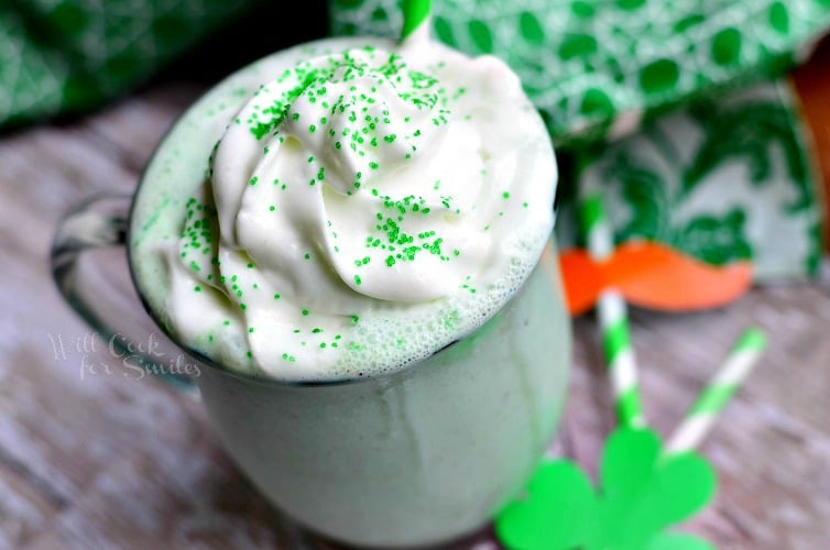 St. Patrick's Day Milkshake in a glass cup with whip cream and green sprinkles on top with a green and white straw