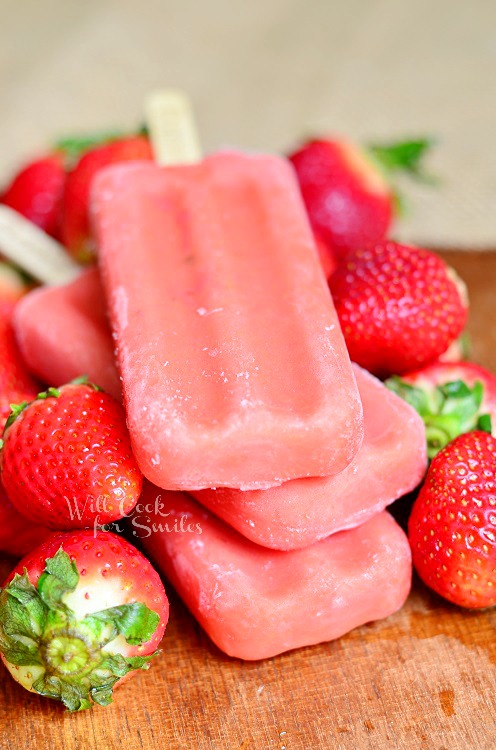 Strawberry Outshine Bars stacked up on a wood cutting board with strawberries around it 