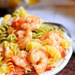 chipotle shrimp and bacon tomato pasta bowl on a decorative white plate on red cloth with a fork at top of plate