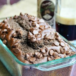 clear glass baking dish with chocolate stout bread on a tan cloth on wood table with clear glass beer mug half full with stout and a bottle of stout in the background