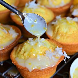coconut lemon pound cake muffins on cooling rack on wood table as a spoon drizzles coconut syrup over first muffin in foreground