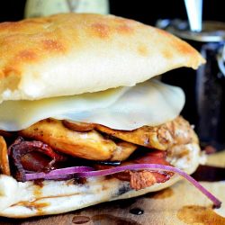 close up view of guinnes glaze chicken sandwich on a wood cutting board with jar of guinness sauce in background to the right