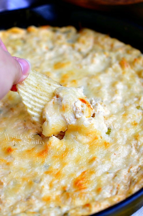 cooked spicy chicken ranch dip in a black skillet with a hand pulling a chip with dip on it into view