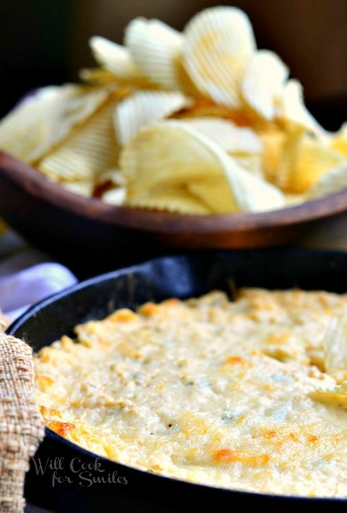 Spicy Chicken Ranch Dip in a cast iron skillet with chips in a wood bowl in the background 