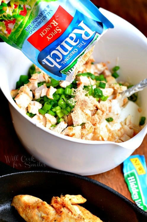 pouring ranch mix into bowl with chicken and green onions 