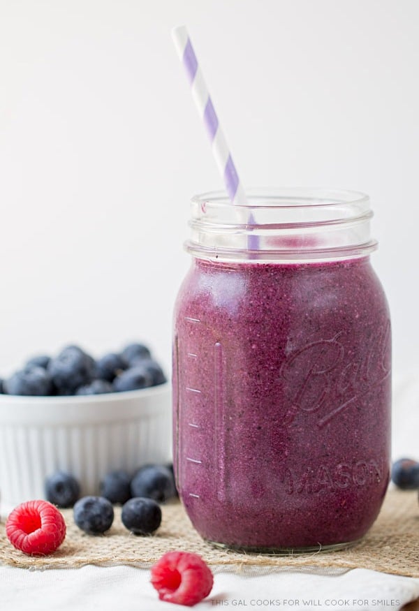 berry smoothy in a mason jar and a bowl of blueberries to the left 