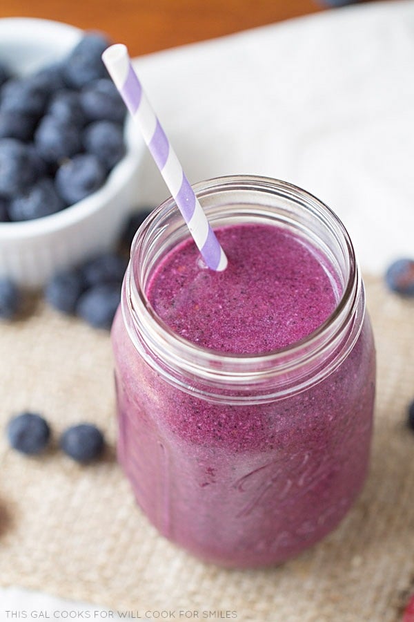top view berry smoothy in a mason jar and a bowl of blueberries to the left 