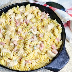 above view of skillet with chicken cordon bleu pasta dish on a brown cloth and a spoon in the upper right of picture