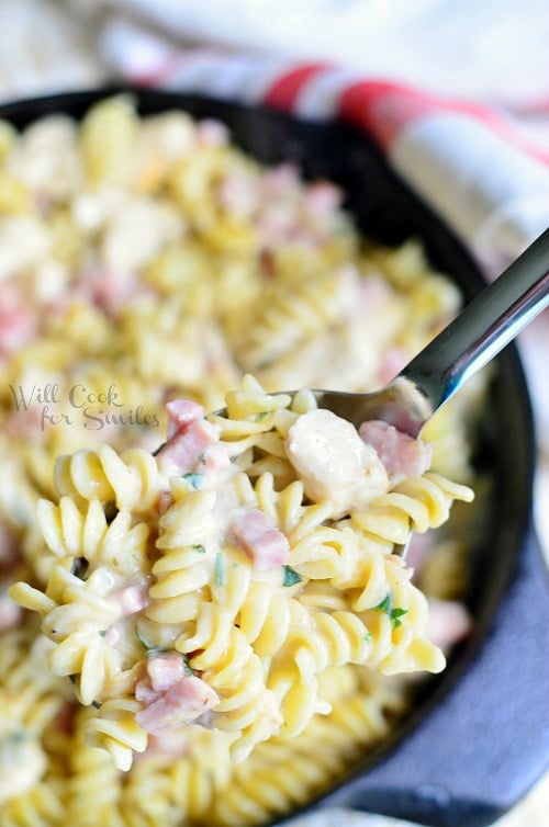 lifting Chicken Cordon Bleu Pasta out of cast iron pan with a metal spoon 