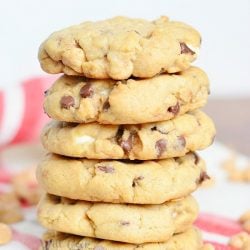 6 gooey loaded peanut butter cookies stacked on a white and red placemat with peanut butter chips scattered at base of stack