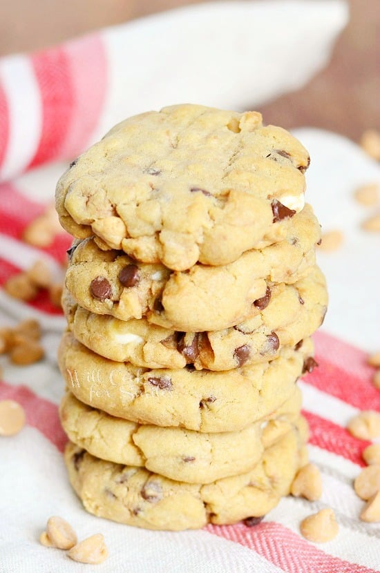 Peanut Butter Cookies that are loaded with white chocolate chips, mini chocolate chips and peanut butter morsels stacked up on a white and red kitchen towel 