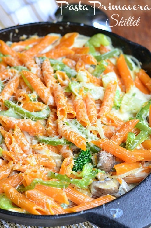 baked pasta primavera in a skillet on a brown colored cloth on wood table