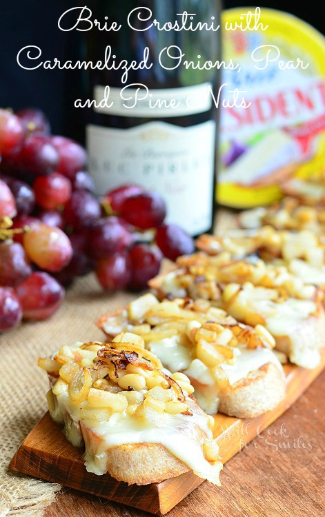 Brie Crostini with Caramelized Onions, Pear and Pine Nuts on a wood board 