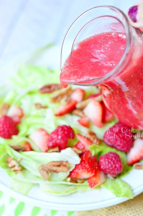 pouring Raspberry Lime Vinaigrette over salad with berries 